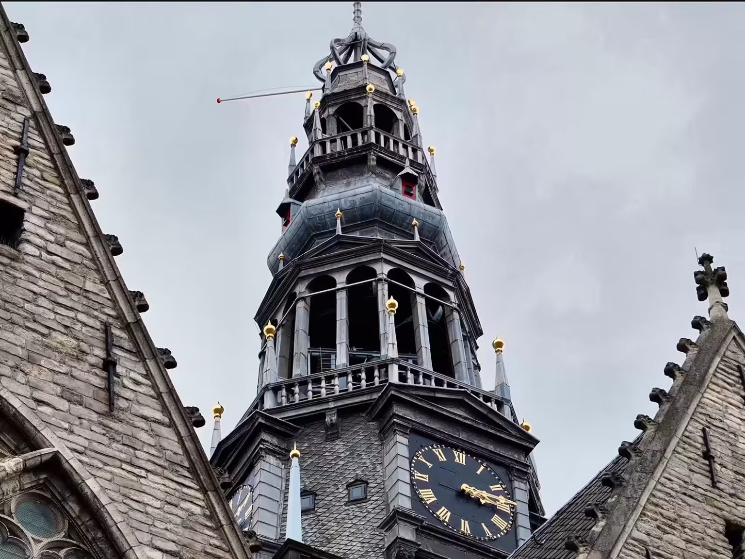 The towering spire of the Oude Kerk displays intricate architecture and a large clock face set against a grey sky