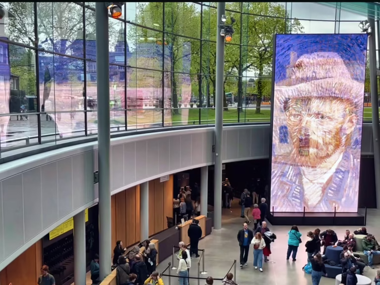 A large digital display featuring van gogh's art greets visitors in the modern interior of the Van Gogh Museum
