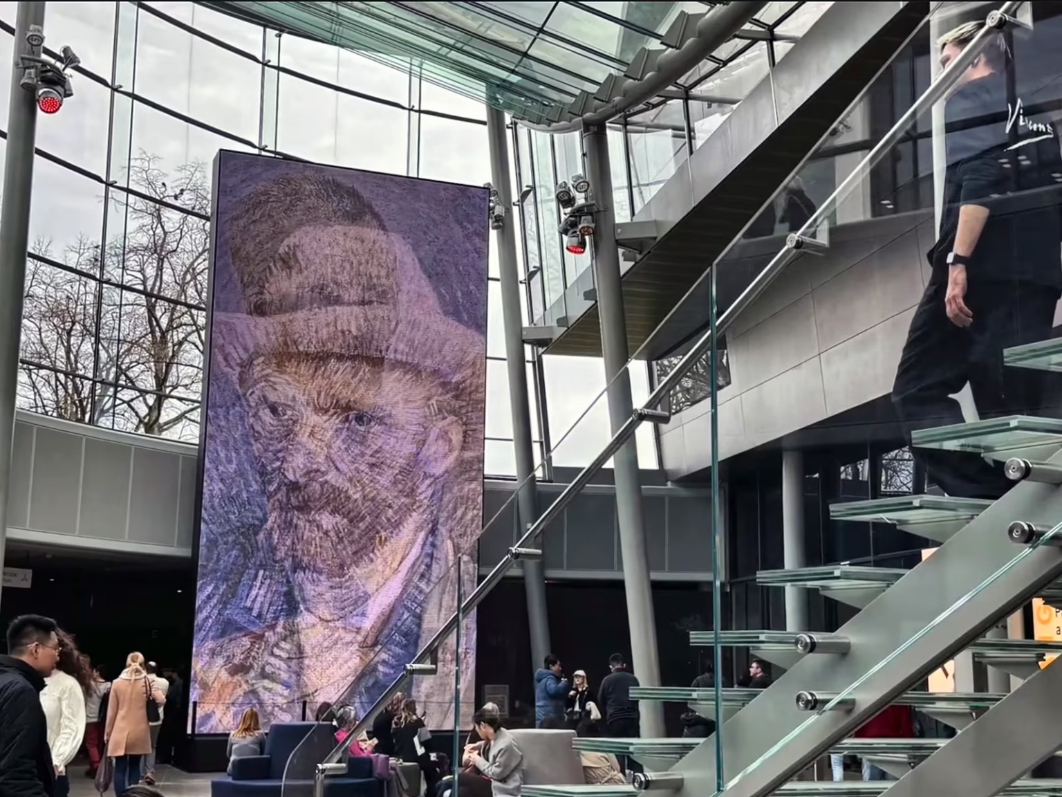 Inside the Van Gogh Museum visitors admire a large projection of a self-portrait while others interact and explore the space