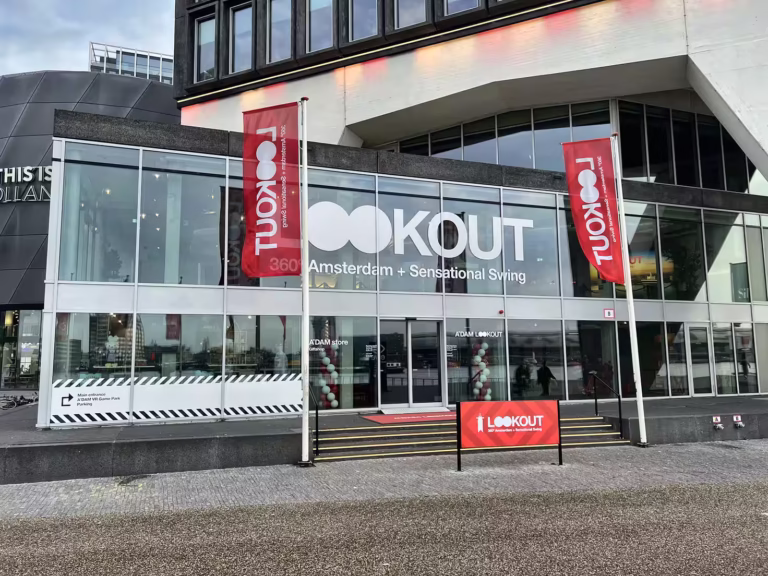 A’DAM Lookout is a modern attraction in amsterdam featuring a large glass entrance and flags inviting visitors to experience