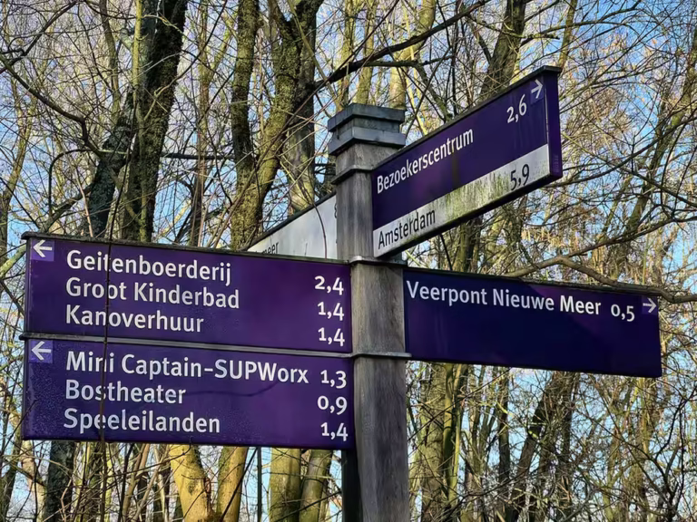 The Amsterdamse bos signpost displays directions to various attractions and distances in a wooded area