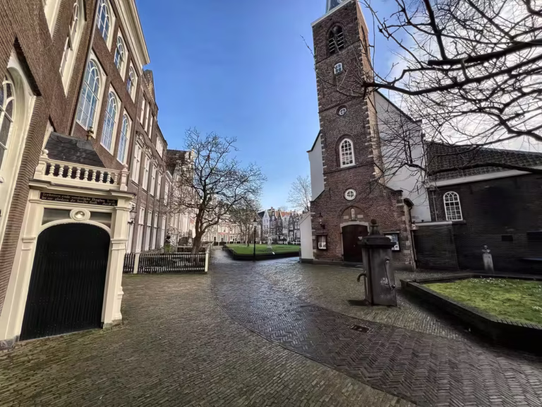 A peaceful scene in Begijnhof featuring historical buildings and a church near a green space