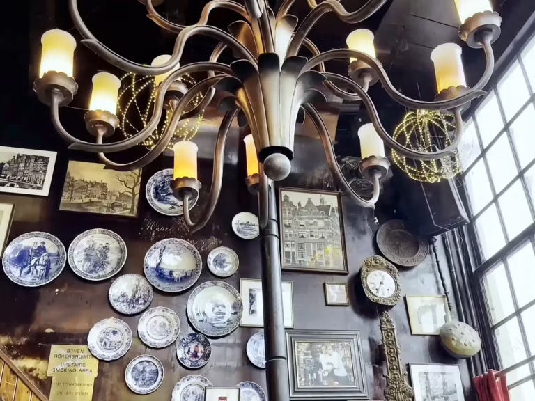 A decorative chandelier hangs from the ceiling in a cozy Brown cafe adorned with vintage plates and various wall art