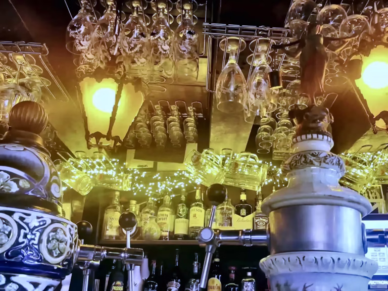 A cozy Brown cafe interior features a beautifully arranged bar with glassware and lighted bottles glowing softly