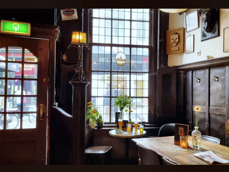 A cozy corner of a Brown cafe featuring wooden accents a small round table with drinks and flowers and large windows letting
