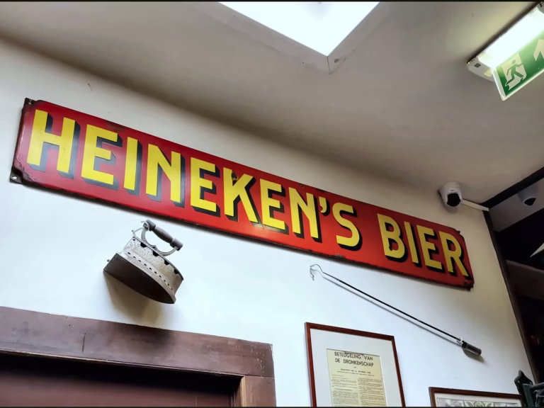 The vintage sign reading heineken's bier is prominently displayed on the wall inside a Brown cafe with eclectic decor