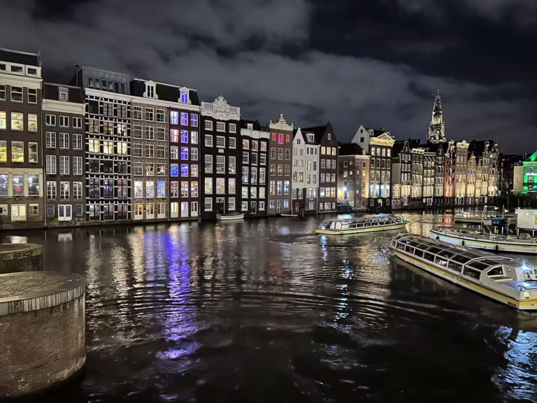 The scenic view showcases the beautiful Canals Amsterdam lined with historic buildings lit at night creating a vibrant atmosp