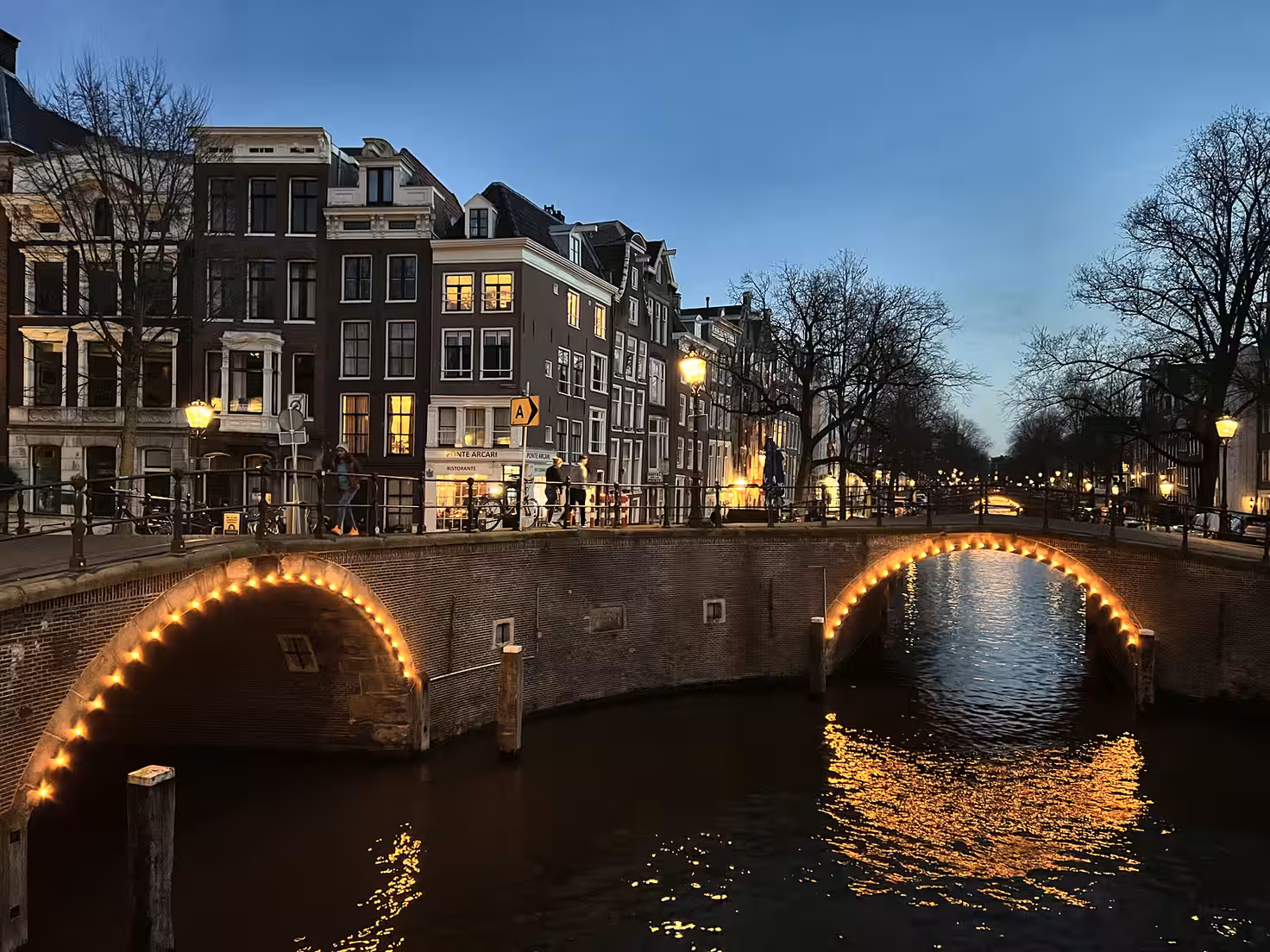 At twilight in amsterdam soft lamplight glows along the canal and bridge reflecting beautifully in the water a serene view of