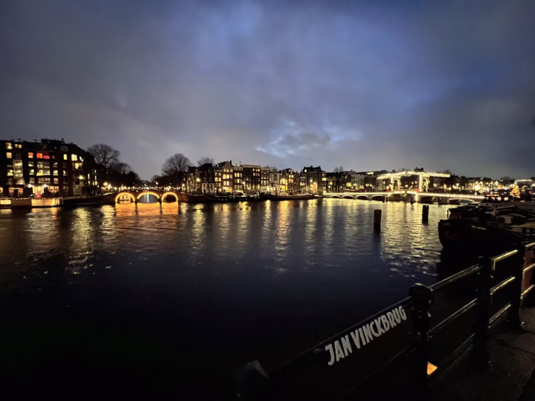 The scene captures the serene beauty of the Canals Amsterdam at dusk with lights reflecting on the water's surface