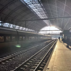 The view of Centraal Station shows platforms illuminated by the sun with a train in the background and passengers waiting