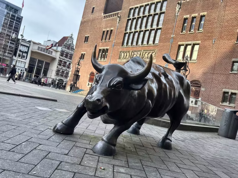 A striking bronze bull sculpture stands prominently on Damrak surrounded by historic buildings and bustling pedestrians