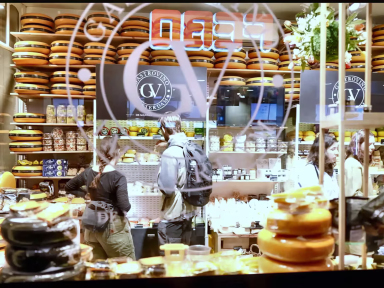 People are shopping in a vibrant cheese store with various cheese types displayed prominently in the De wallen area