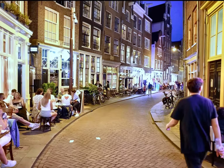 A lively evening scene in De wallen shows people sitting at cafés and walking along the cobbled street