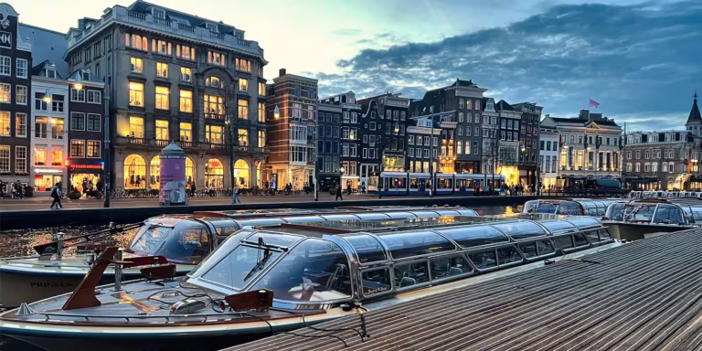 As the evening falls boats lined up along the canal invite visitors to discover the beautiful architecture and lights of Amsterdam