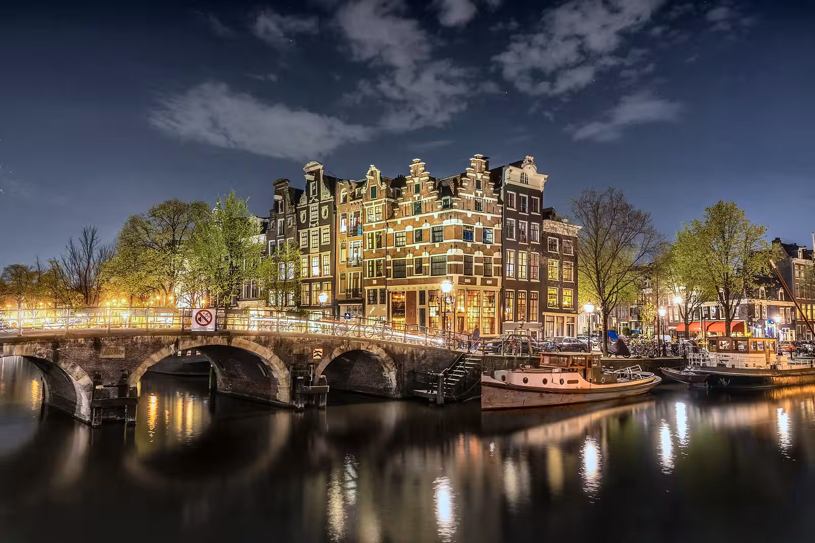Discover the beauty of Amsterdam at night with illuminated buildings reflecting on the water of a serene canal