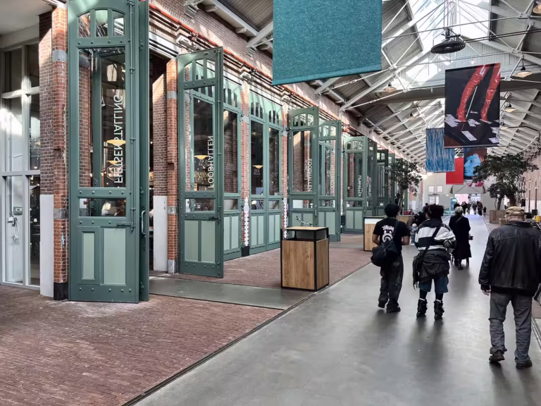 The interior of Foodhallen Amsterdam showcases a spacious corridor lined with large open doors leading to various food stalls