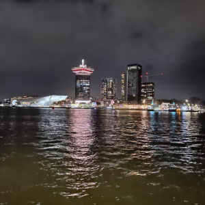 A nighttime view of Het IJ with city lights reflecting on the water and prominent buildings in the background