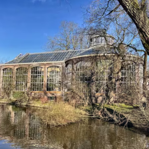A scenic view of the Hortus Botanicus Amsterdam greenhouse by the water surrounded by nature and trees