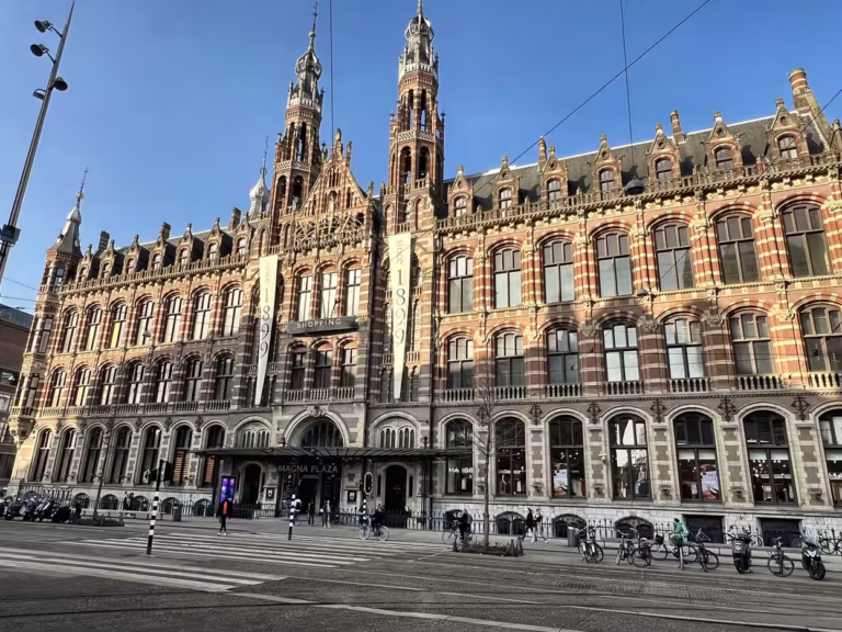 The beautiful facade of Magna Plaza displays intricate architecture with tall spires and vibrant colors under a clear blue sk