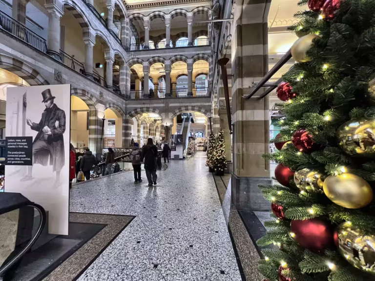 The interior of Magna Plaza features festive decorations with christmas trees and shoppers admiring the architecture