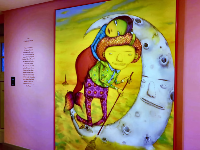 The vibrant mural at the Moco museum features whimsical characters riding a crescent moon surrounded by surreal scenery