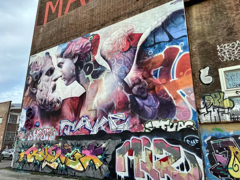 A large mural featuring vibrant colors and detailed faces dominates the wall at NDSM Wharf showcasing artistic expression