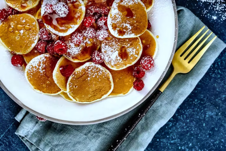 Delicious pancakes topped with powdered sugar and fresh raspberries are nestled on a white plate showcasing Pancake houses - food & drinks