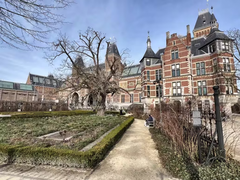 The view showcases the beautifully designed Rijksmuseum building surrounded by a green garden area and clear sky