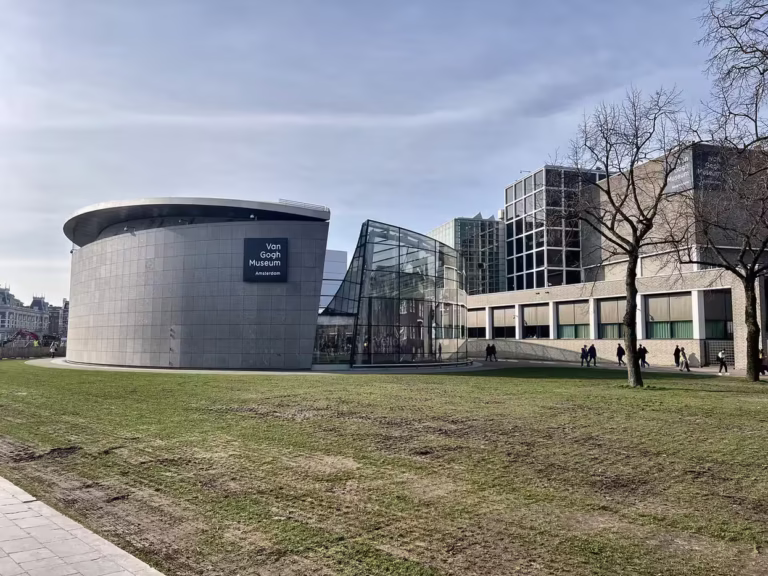 The Van Gogh Museum features modern architecture with a sleek glass entrance and a round stone structure set in a grassy area